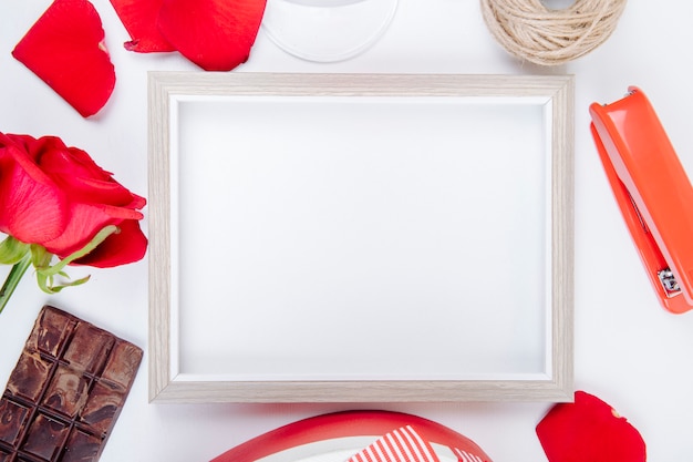 Kostenloses Foto draufsicht eines leeren bilderrahmens mit einer kugel der roten farbe rose und der dunklen schokolade und des hefters des seils auf weißem hintergrund mit kopienraum