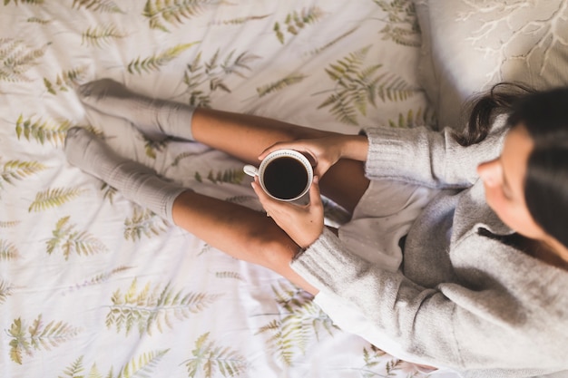 Kostenloses Foto draufsicht eines mädchens, das auf dem bett hält tasse kaffee sitzt