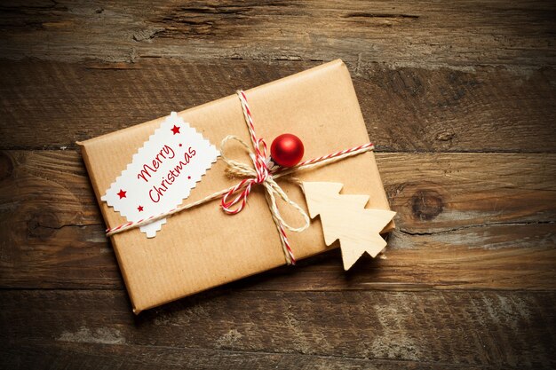 Draufsicht eines verpackten Weihnachtsgeschenks mit einer Karte, die frohe Weihnachten liest, auf einer hölzernen Oberfläche