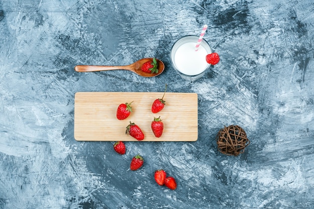 Draufsicht Erdbeeren auf Schneidebrett mit Milch, Clew und einem Holzlöffel auf dunkelblauer Marmoroberfläche. horizontal