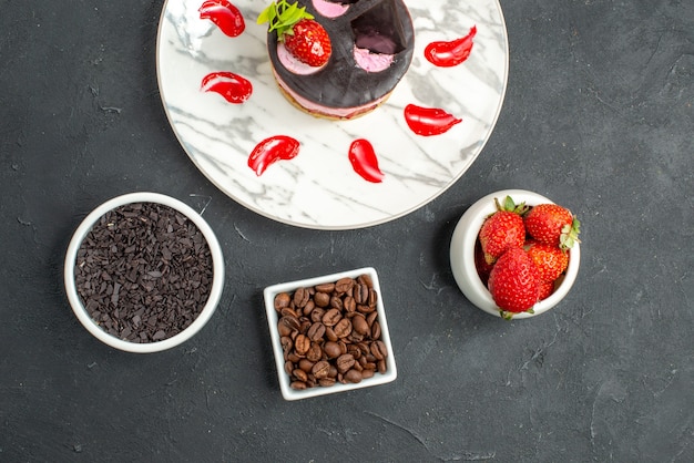 Kostenloses Foto draufsicht erdbeerkäsekuchen auf weißen ovalen tellerschalen mit erdbeeren und schokolade auf dunklem hintergrund