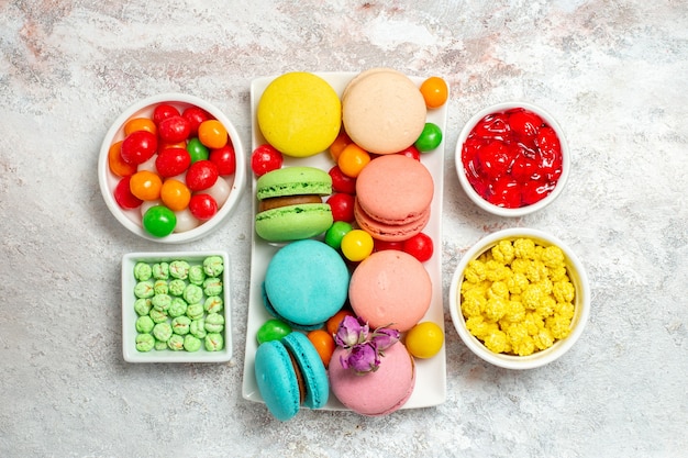 Draufsicht färbte köstliche Macarons kleine Kuchen mit Bonbons auf weißem Raum