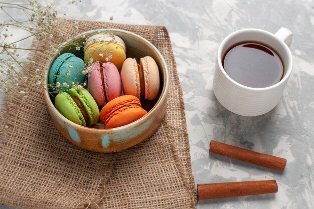 Draufsicht farbige französische Macarons köstliche kleine Kuchen mit Tasse Tee auf weißer Oberfläche