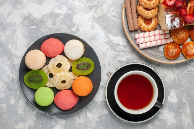 Draufsicht farbige kleine Kuchen mit Tasse Teeplätzchen und Erdbeerkuchen auf hellweißer Oberfläche