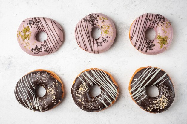 Draufsicht flache Laienansicht vieler Schokoladen- und rosa Donuts auf weißer Oberfläche.