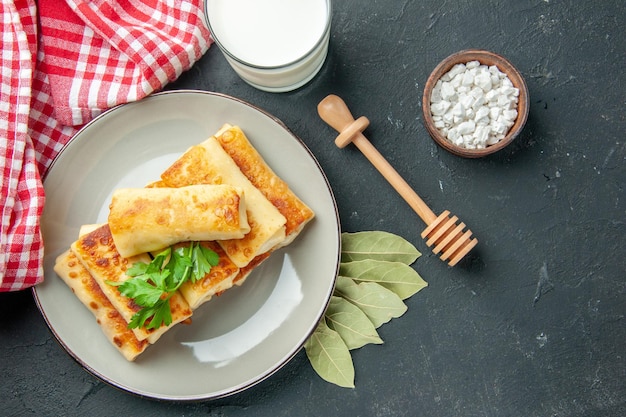 Draufsicht Fleisch gefüllte Blini auf rundem Teller Meersalz in kleiner Schüssel Lorbeerblätter Honig Stick Buttermilch Glas auf dem Tisch