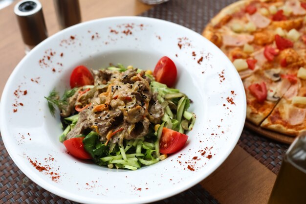 Draufsicht Fleischsalat mit geschnittenen Gurken und Tomaten auf einem Teller mit Gewürzen