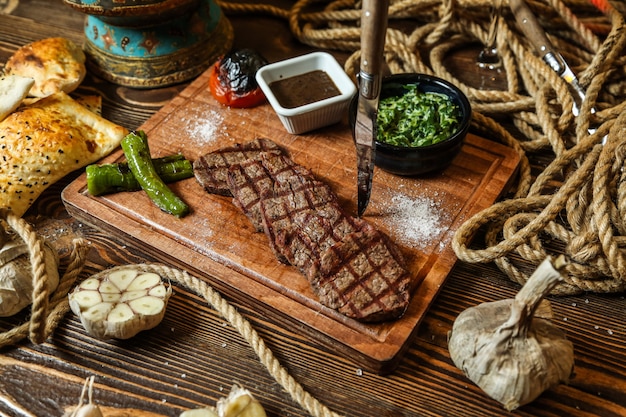 Draufsicht Fleischsteak mit gegrillter Tomate und Peperoni mit Saucen auf einem Ständer mit Knoblauch