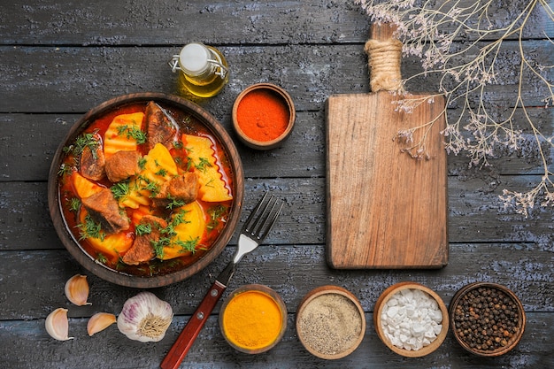 Draufsicht Fleischsuppe mit Kartoffeln und Gewürzen auf dunklem Schreibtisch