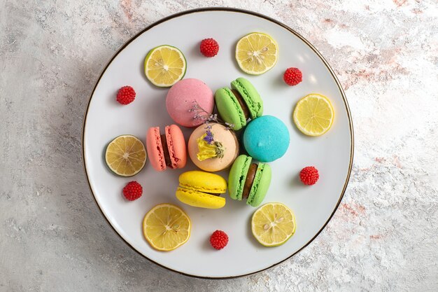 Draufsicht französische Macarons kleine köstliche Kuchen mit Zitronenscheiben auf einem weißen Oberflächenkuchenplätzchenzuckerplätzchen süß