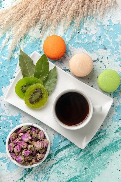 Draufsicht französische Macarons köstliche kleine Kuchen mit Tasse Tee auf hellblauem Oberflächenkuchen backen Keks süßer Zuckerkuchen-Tee