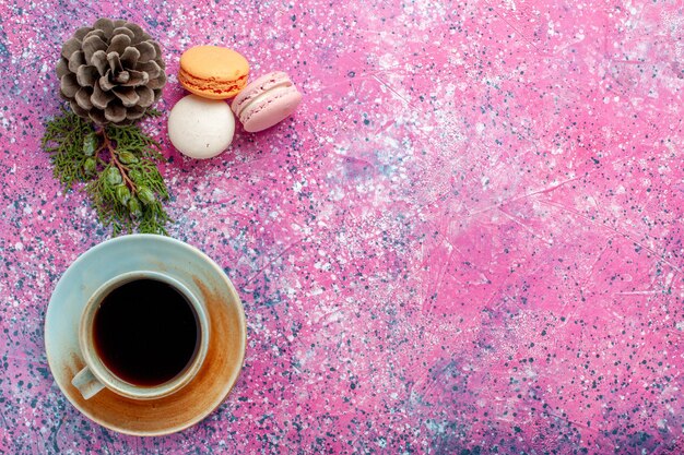 Draufsicht französische Macarons köstliche kleine Kuchen mit Tasse Tee auf rosa Oberfläche