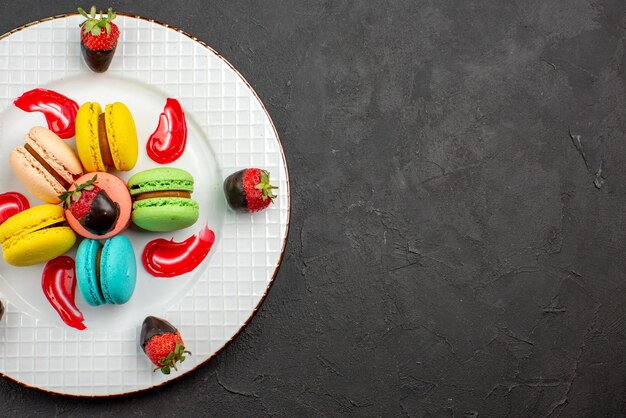 Draufsicht Französische Makronen appetitlich mit Schokolade überzogene Erdbeeren und französische Makronen auf dem dunklen Tisch