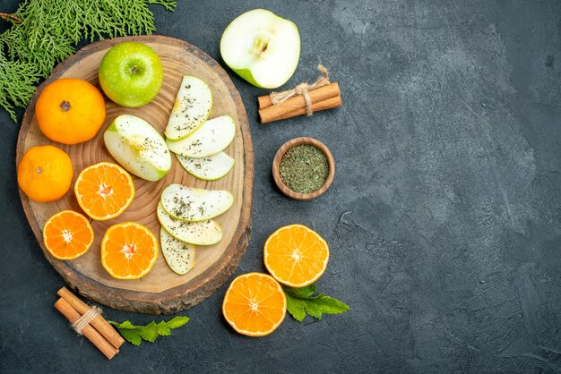 Draufsicht frisch geschnittene äpfel und orangen getrocknetes minzpulver in schüssel zimtstangen auf holzbrett auf schwarzem tisch