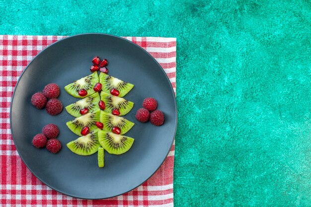 Draufsicht frisch geschnittene Kiwis mit Himbeeren auf grünem Hintergrund