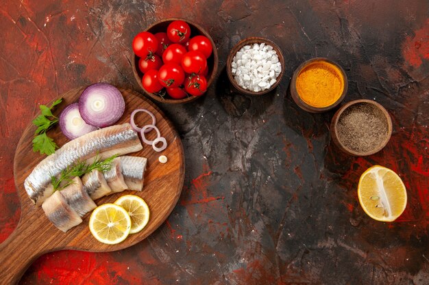 Draufsicht frisch geschnittener Fisch mit Gewürzen Zwiebelringen und frischen Tomaten auf dunklem Hintergrund