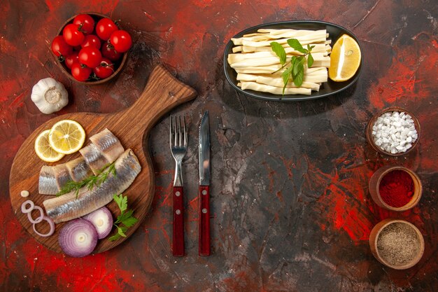 Draufsicht frisch geschnittener Fisch mit Zwiebelringen Tomaten und Gewürzen auf dunklem Schreibtisch Farbfoto Fleischsnack Meeresfrüchtemahlzeit