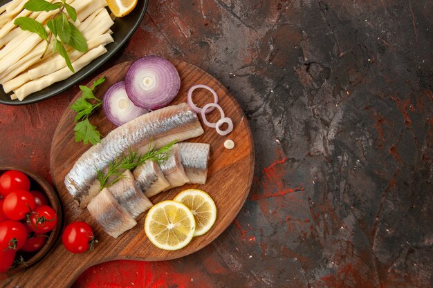 Draufsicht frisch geschnittener Fisch mit Zwiebelringen und frischen Tomaten auf dunklem Hintergrund