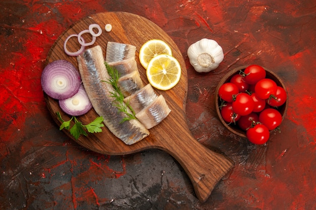 Draufsicht frisch geschnittener Fisch mit Zwiebelringen und Tomaten auf dunklem Hintergrund