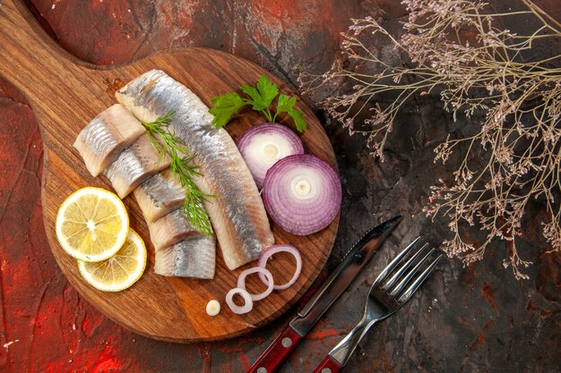 Draufsicht frisch geschnittener Fisch mit Zwiebelringen und Zitrone auf dunklem Hintergrund