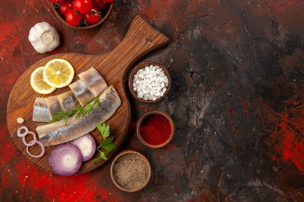 Draufsicht frisch geschnittener Fisch mit Zwiebelringtomaten und Gewürzen auf dunklem Hintergrund