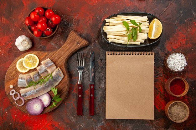 Draufsicht frisch geschnittener Fisch mit Zwiebelringtomaten und Gewürzen auf dunklem Hintergrund