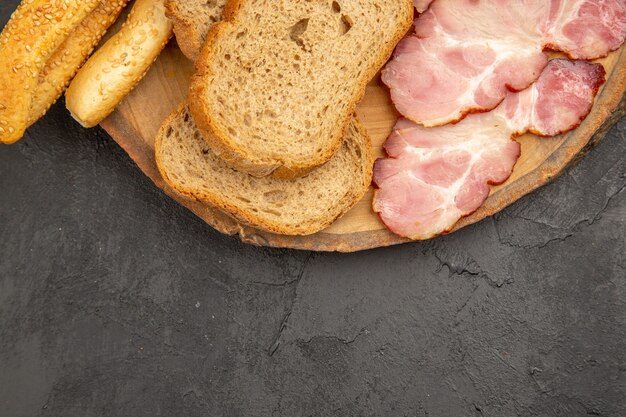 Draufsicht frisch geschnittener Schinken mit Brötchen und Brotscheiben auf dunklem Hintergrund