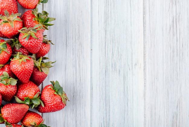 Draufsicht frische Erdbeere auf der linken Seite mit Kopienraum auf weißem hölzernem Hintergrund