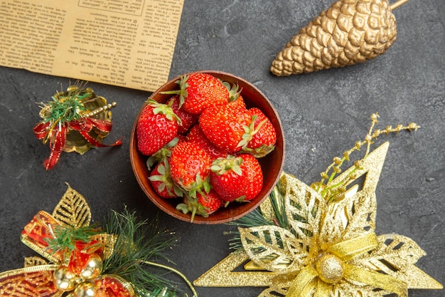 Draufsicht frische Erdbeeren im Teller um Weihnachtsspielzeug auf dunklem Hintergrund