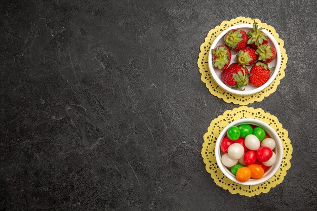 Draufsicht frische Erdbeeren mit bunten Bonbons auf dunklem Hintergrund Fruchtbeerenfarbe Regenbogensüßigkeit