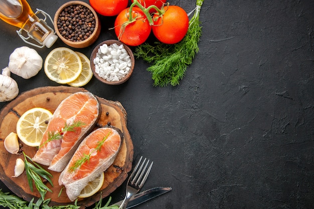 Draufsicht frische Fischscheiben mit Gewürzen und Zitronenscheiben auf dunklem Tisch