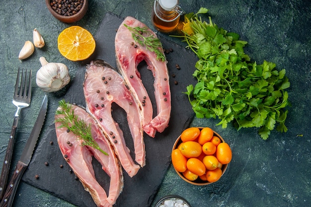 Draufsicht frische Fischscheiben mit Grüns und Kumquats auf dunkelblauem Hintergrund