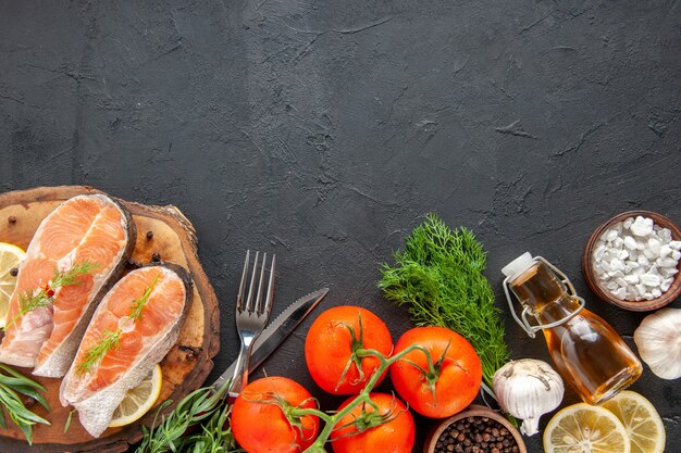 Draufsicht frische Fischscheiben mit Tomatengewürzen und Zitronenscheiben auf dem dunklen Tisch