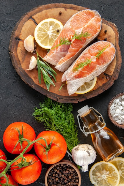 Draufsicht frische Fischscheiben mit Tomatengewürzen und Zitronenscheiben auf dem dunklen Tisch