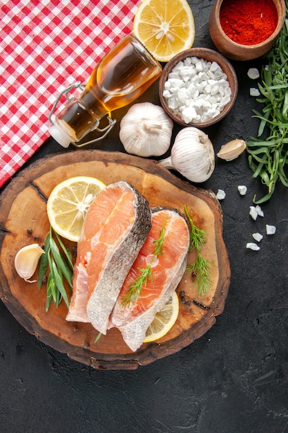 Draufsicht frische Fischscheiben mit Zitronenscheiben Knoblauch und Gewürzen auf dunklem Tisch