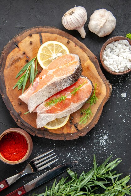 Draufsicht frische Fischscheiben mit Zitronenscheiben und Gewürzen auf dunklem Tisch