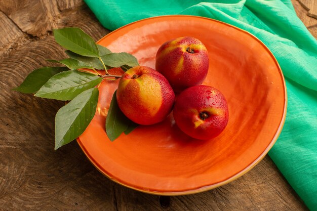 Draufsicht frische ganze Pfirsiche innerhalb der orange Platte auf der braunen hölzernen Schreibtischfruchtsaft-Sommerfarbe