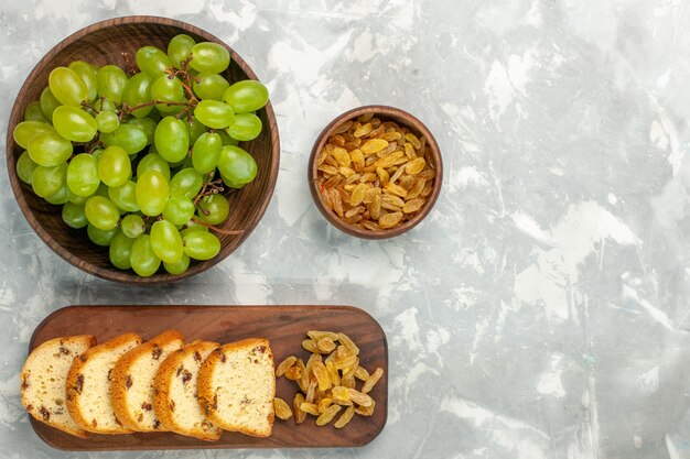 Draufsicht frische grüne Trauben mit Rosinen und Kuchenscheiben auf hellweißem Schreibtisch