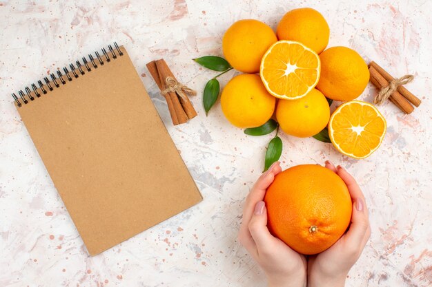 Draufsicht frische Mandarinen-Zimtstangen, die in Frauenhänden ein Notizbuch auf heller isolierter Oberfläche orange geschnitten werden