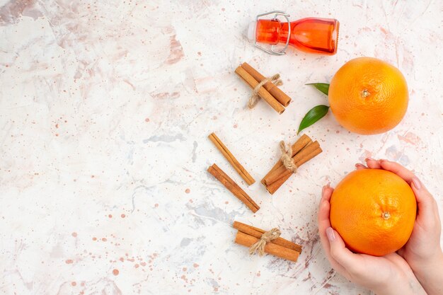 Draufsicht frische Orangen Zimtstangen orange in weiblicher Handflasche auf hellem oberflächenfreiem Platz