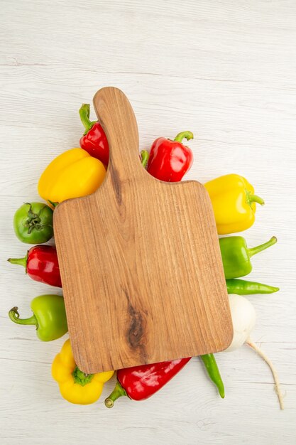 Draufsicht frische Paprika unterschiedlich gefärbt mit braunem Holzschreibtisch auf weißem Hintergrund Salat reife Fotomahlzeit Farbe