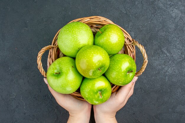 Draufsicht frische Äpfel im Weidenkorb in weiblicher Hand auf dunkler Oberfläche