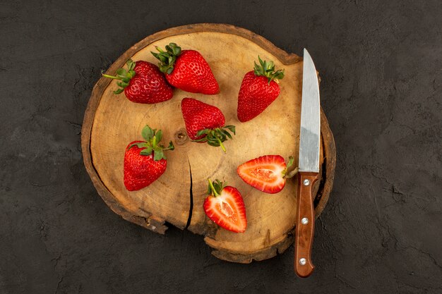 Draufsicht frische rote Erdbeeren in Scheiben geschnitten weich reif auf dem braunen Schreibtisch und dunkel