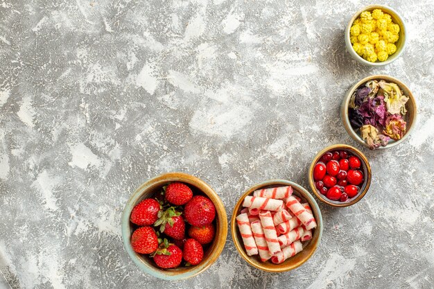 Draufsicht frische rote Erdbeeren mit Bonbons auf weißer Oberfläche Frucht süße Bonbonfarbe