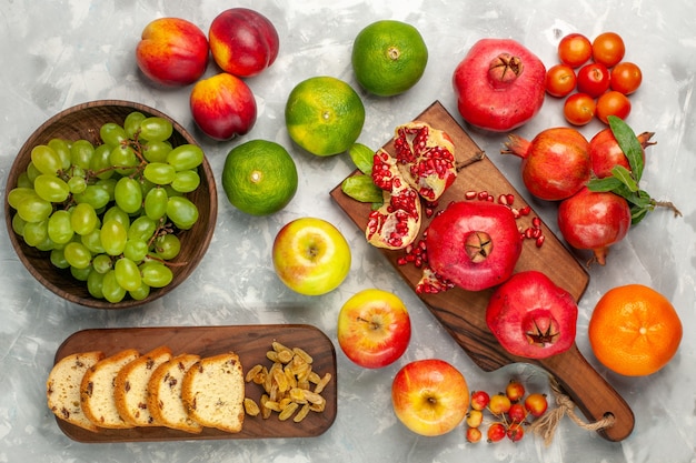 Draufsicht frische rote Granatäpfel mit Mandarinenkuchen und Äpfeln auf dem hellweißen Schreibtisch