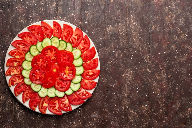 Draufsicht frische rote Tomaten geschnitten mit Gurken frischem Salat auf dem braunen Raum