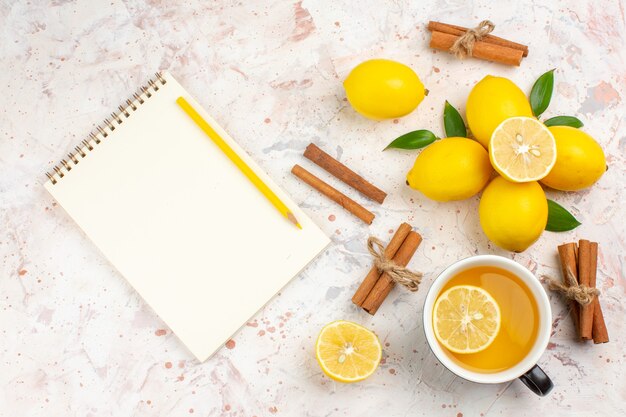 Draufsicht frische Zitronen geschnitten Zitronenzimtstangen eine Tasse Zitronentee Notizbuch auf helle isolierte Oberfläche