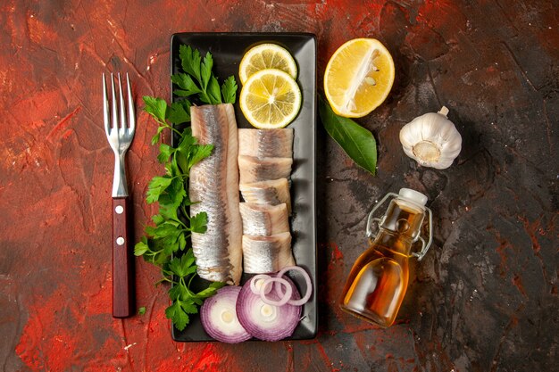 Draufsicht frischer Fisch in Scheiben geschnitten mit grüner Zitrone und Zwiebel in schwarzer Pfanne auf dunklem Hintergrund