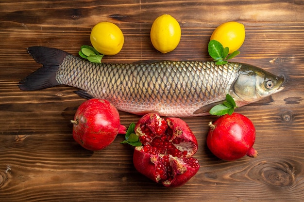 Kostenloses Foto draufsicht frischer fisch mit granatäpfeln und zitrone auf holzschreibtisch
