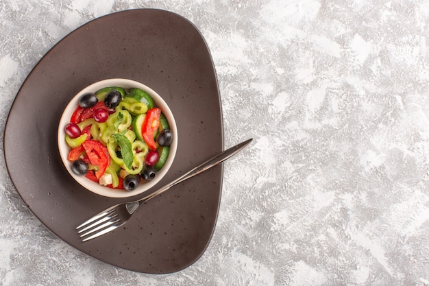 Draufsicht frischer Gemüsesalat mit geschnittenen Gurkentomaten-Oliven- und Weißkäse in brauner Platte auf dem grauen rustikalen Schreibtischgemüsesalat-Salatmehl